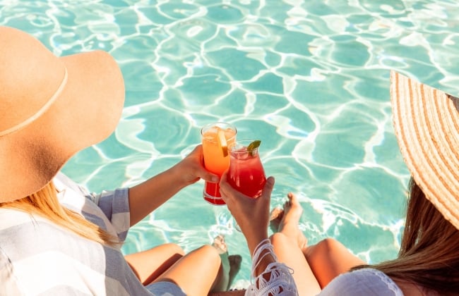 image of two women holding drinks poolside